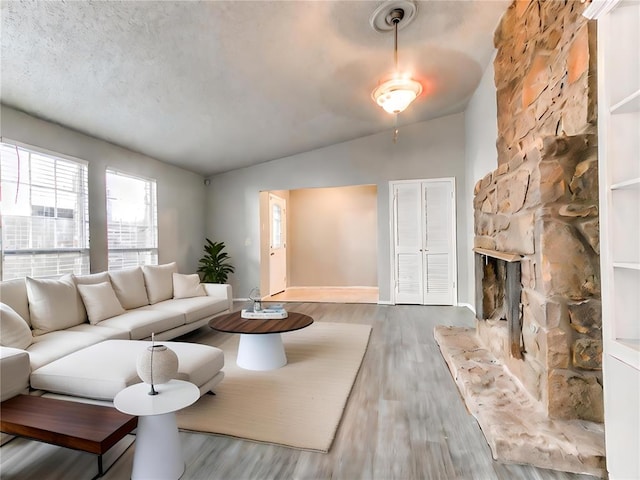 living room featuring a stone fireplace, hardwood / wood-style floors, lofted ceiling, and a textured ceiling