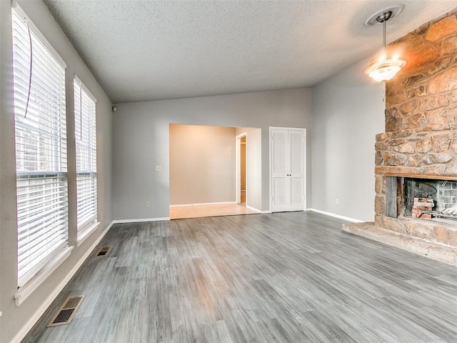 unfurnished living room featuring hardwood / wood-style flooring, vaulted ceiling, a textured ceiling, and a fireplace