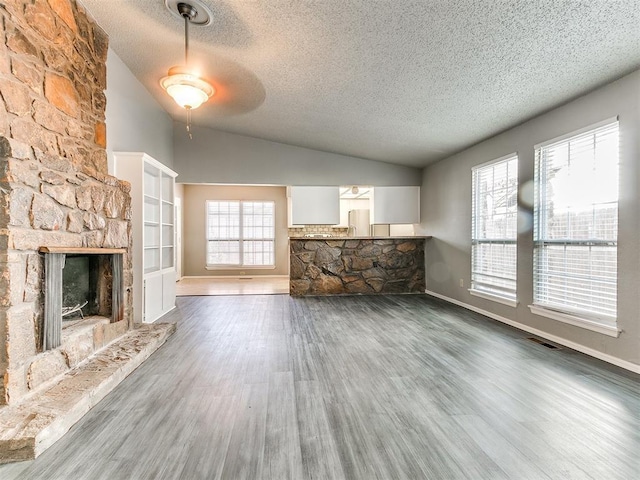 unfurnished living room with lofted ceiling, a stone fireplace, dark hardwood / wood-style flooring, and plenty of natural light