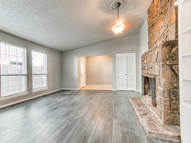 unfurnished living room featuring lofted ceiling, hardwood / wood-style flooring, a fireplace, and a textured ceiling