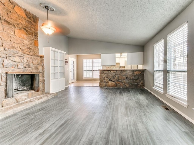 unfurnished living room featuring vaulted ceiling, dark wood-type flooring, a wealth of natural light, and a fireplace