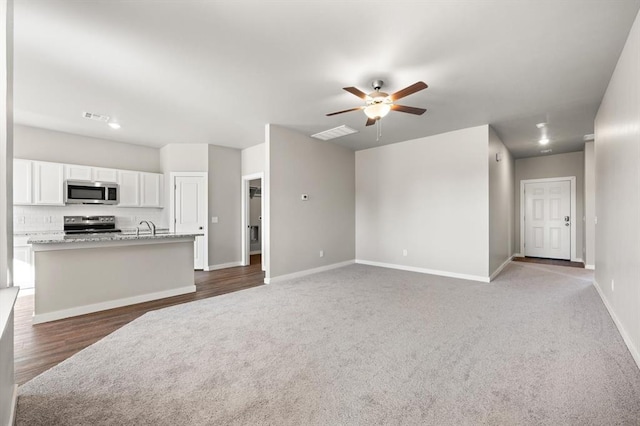 unfurnished living room with dark carpet, ceiling fan, and sink