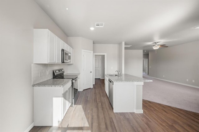 kitchen with stainless steel appliances, white cabinetry, light stone countertops, and a center island with sink