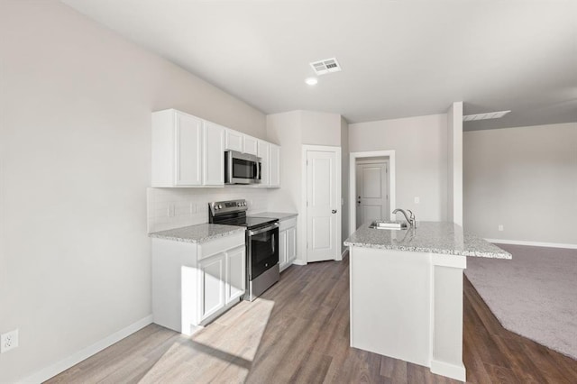 kitchen featuring appliances with stainless steel finishes, sink, white cabinets, a kitchen island with sink, and light stone countertops