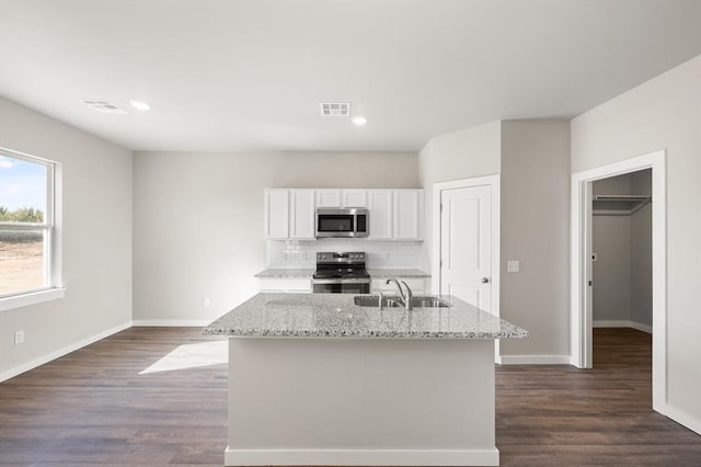 kitchen featuring white cabinetry, stainless steel appliances, light stone counters, and a center island with sink