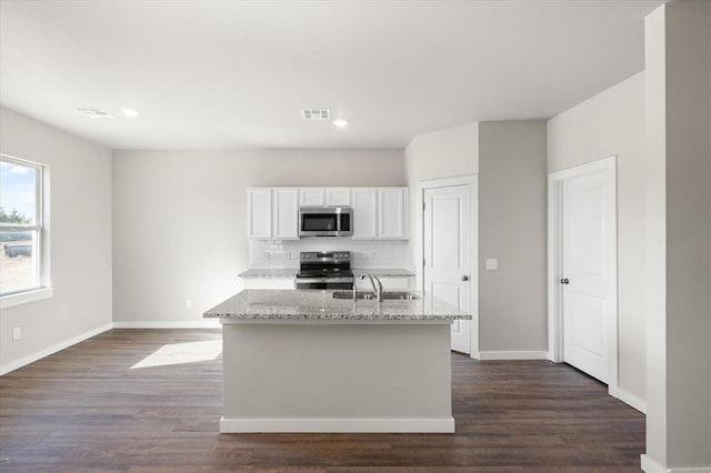 kitchen with stainless steel appliances, light stone counters, tasteful backsplash, white cabinets, and a center island with sink