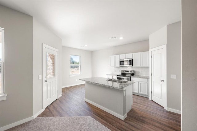 kitchen featuring appliances with stainless steel finishes, dark hardwood / wood-style floors, white cabinetry, light stone countertops, and a center island with sink