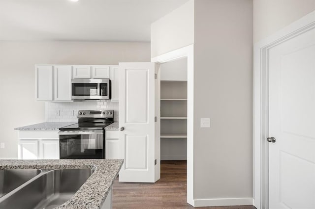 kitchen featuring appliances with stainless steel finishes, light stone counters, wood-type flooring, white cabinets, and decorative backsplash