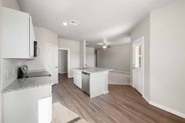 kitchen with sink, appliances with stainless steel finishes, white cabinetry, light stone counters, and a center island with sink