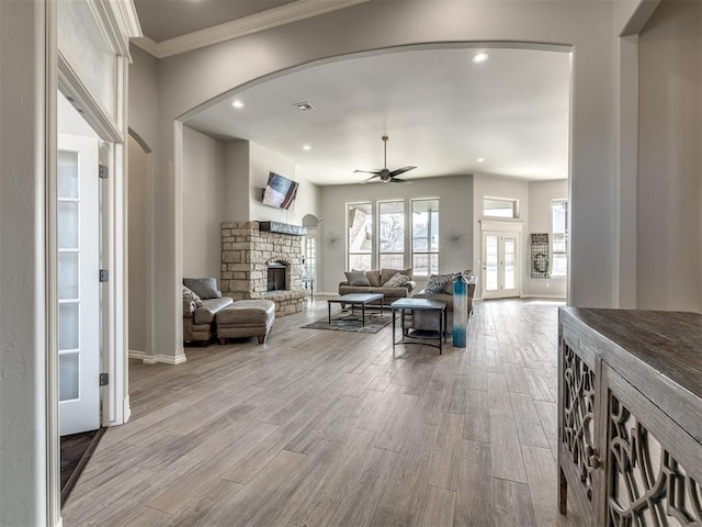 living room featuring a stone fireplace, ornamental molding, light hardwood / wood-style floors, and ceiling fan