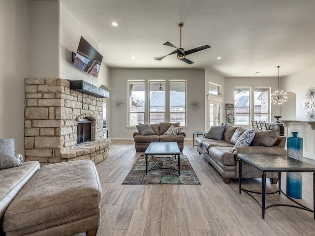 living room featuring ceiling fan with notable chandelier, a fireplace, and light hardwood / wood-style flooring