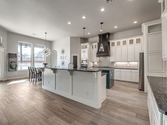 kitchen with a breakfast bar area, custom exhaust hood, a large island with sink, stainless steel appliances, and white cabinets