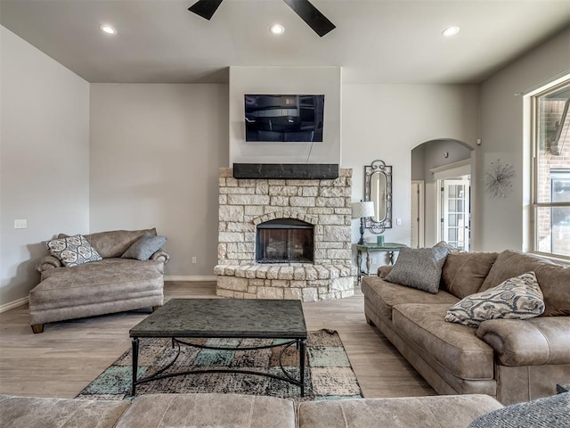 living room featuring a stone fireplace, ceiling fan, and light hardwood / wood-style floors