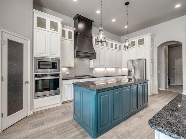 kitchen with a large island, stainless steel appliances, custom range hood, blue cabinets, and dark stone counters