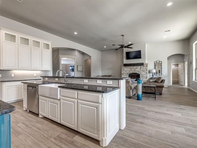 kitchen with white cabinetry, a stone fireplace, sink, and a kitchen island with sink