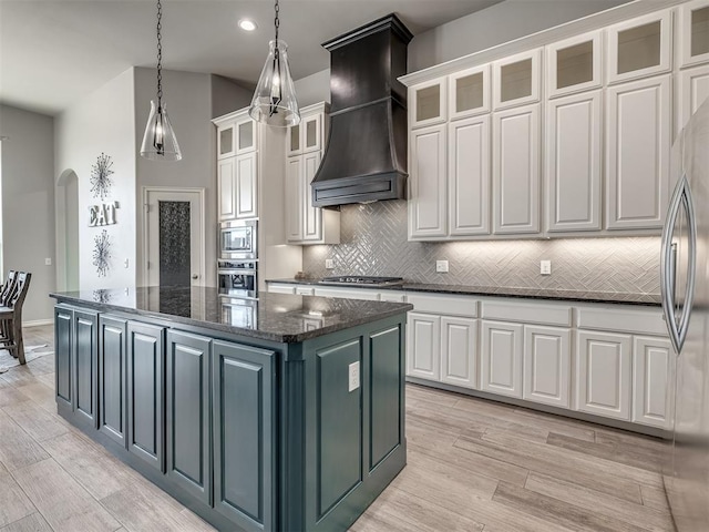 kitchen featuring a kitchen island, appliances with stainless steel finishes, white cabinetry, dark stone counters, and custom exhaust hood