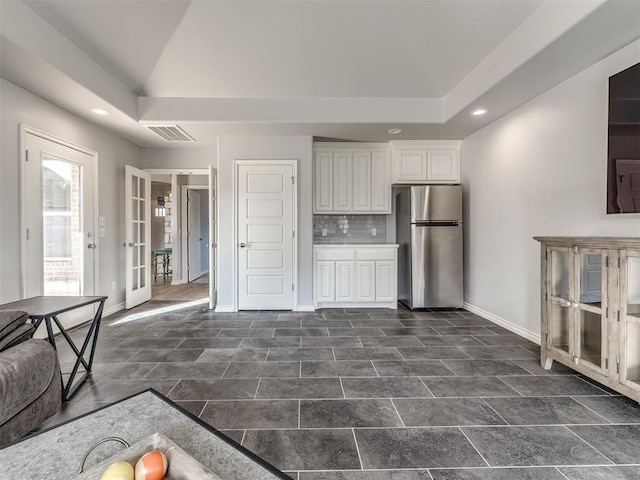 kitchen featuring white cabinets, vaulted ceiling, stainless steel fridge, and decorative backsplash