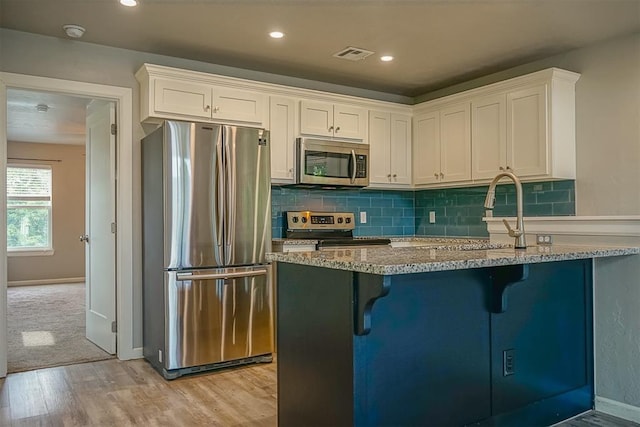 kitchen featuring light stone counters, a kitchen breakfast bar, white cabinets, and appliances with stainless steel finishes