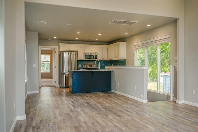 kitchen with appliances with stainless steel finishes, a healthy amount of sunlight, white cabinets, and backsplash