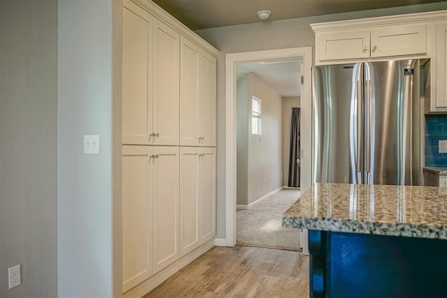 kitchen with tasteful backsplash, light hardwood / wood-style flooring, stainless steel fridge, light stone countertops, and white cabinets