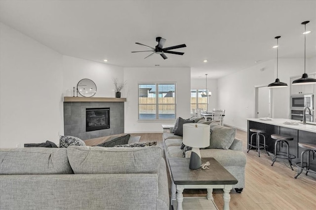 living room featuring a fireplace, ceiling fan with notable chandelier, and light wood-type flooring