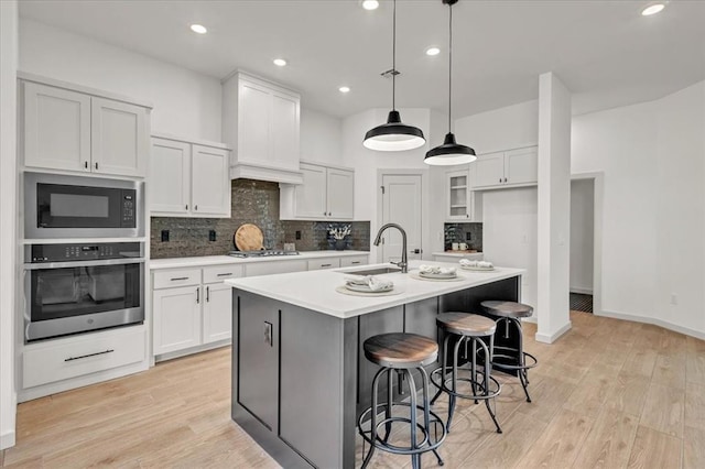 kitchen with sink, decorative light fixtures, a center island with sink, stainless steel appliances, and white cabinets