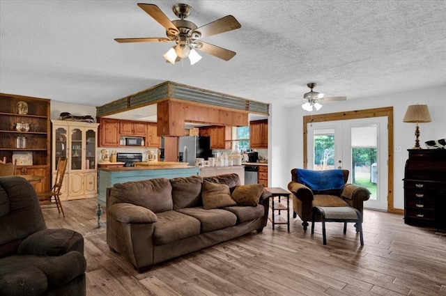 living room with a textured ceiling, light hardwood / wood-style flooring, french doors, and ceiling fan