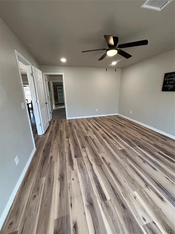 unfurnished room featuring a ceiling fan, visible vents, baseboards, and wood finished floors