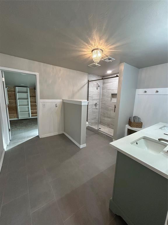 full bath with tile patterned flooring, a sink, visible vents, double vanity, and a stall shower