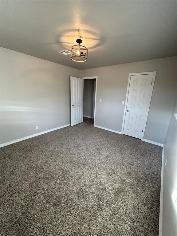 spare room featuring dark colored carpet, visible vents, and baseboards