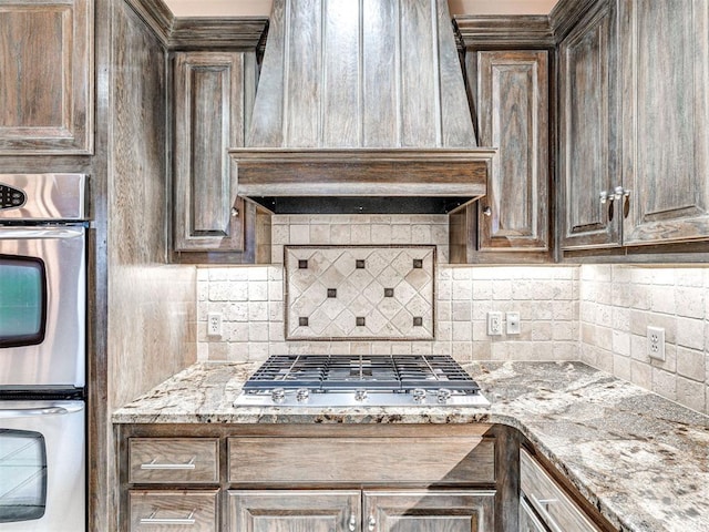 kitchen featuring light stone counters, tasteful backsplash, stainless steel appliances, and premium range hood