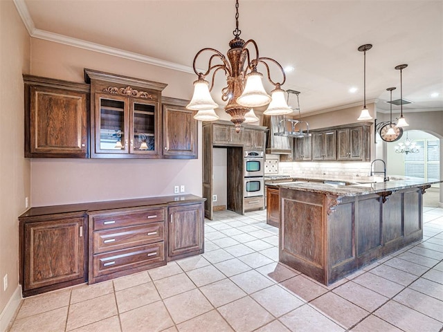 kitchen featuring crown molding, an inviting chandelier, dark brown cabinets, light stone counters, and decorative light fixtures