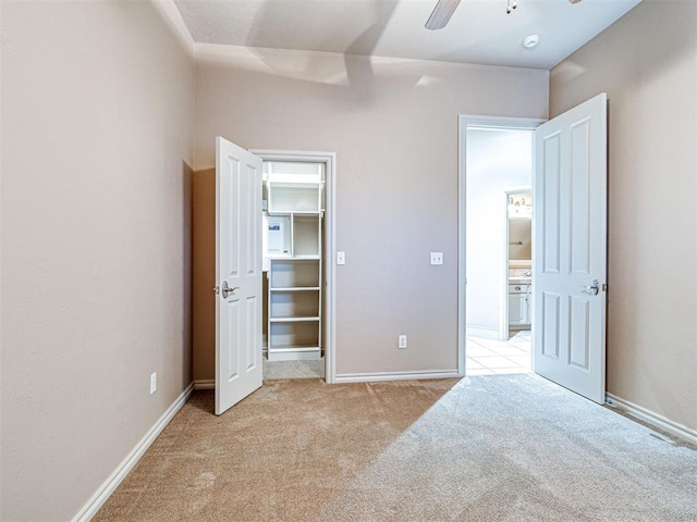 unfurnished bedroom featuring a walk in closet, light carpet, and ceiling fan