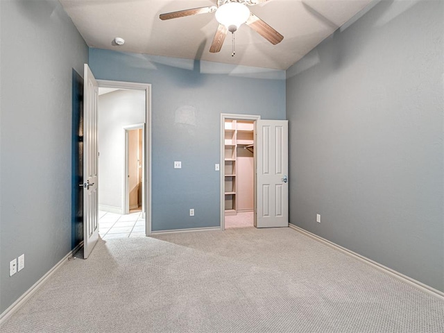 unfurnished bedroom featuring ceiling fan, a walk in closet, a closet, and light carpet