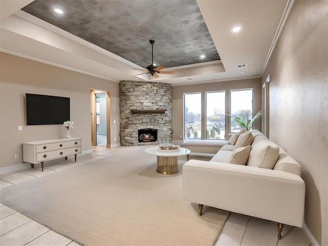 living room with a fireplace, light tile patterned floors, ceiling fan, a raised ceiling, and crown molding