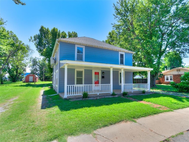 view of front of home featuring a front yard, covered porch, and a storage shed