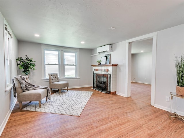 living area featuring a fireplace, light hardwood / wood-style floors, and an AC wall unit