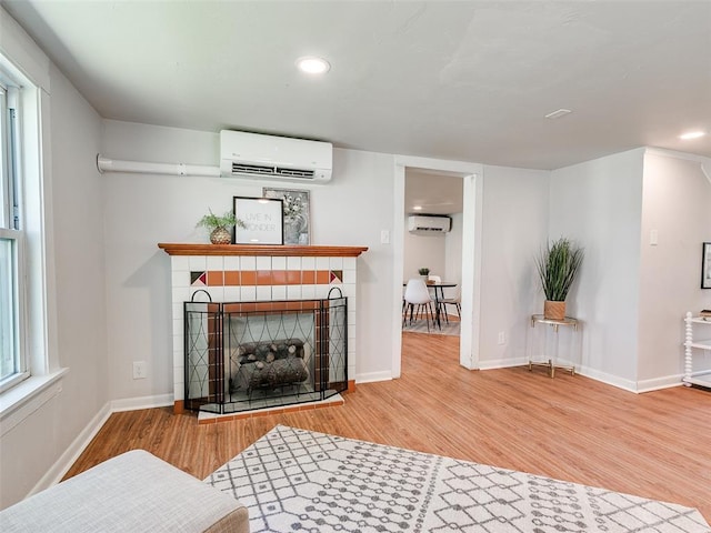 living room featuring a fireplace, hardwood / wood-style floors, and an AC wall unit