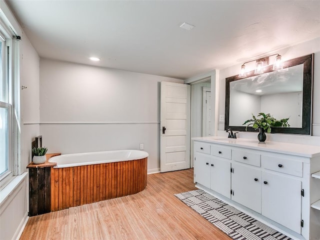 bathroom featuring vanity, a tub to relax in, and wood-type flooring