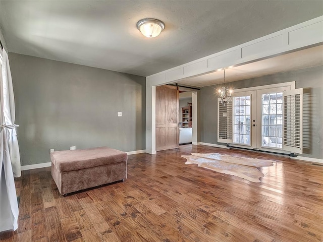 unfurnished room with wood-type flooring, a barn door, and a chandelier