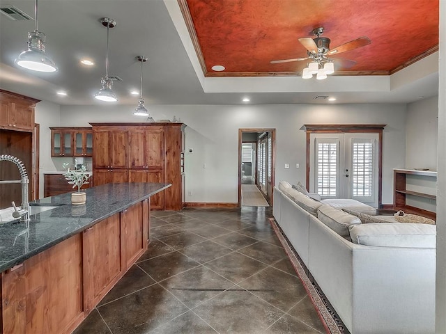 kitchen with ornamental molding, decorative light fixtures, dark stone countertops, and a tray ceiling