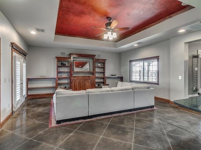 living room with a raised ceiling, plenty of natural light, and ceiling fan