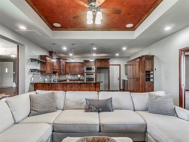 living room with crown molding, sink, ceiling fan, and a tray ceiling