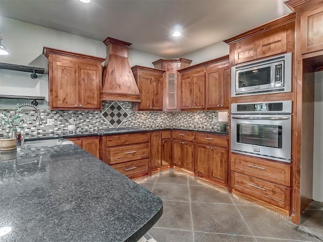 kitchen with premium range hood, appliances with stainless steel finishes, tasteful backsplash, sink, and dark tile patterned floors