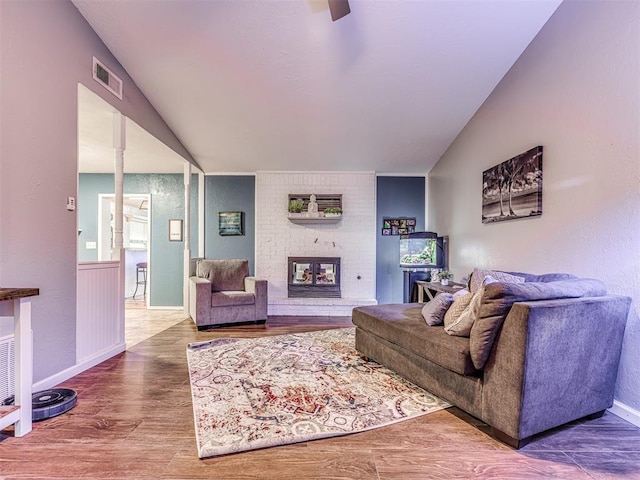 living room with wood-type flooring, vaulted ceiling, and a brick fireplace