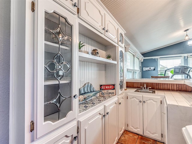 kitchen with white cabinetry, sink, vaulted ceiling, and tile counters