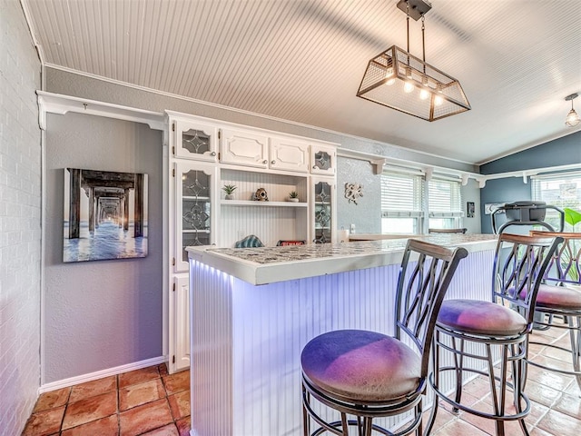 kitchen featuring pendant lighting, brick wall, white cabinets, and a kitchen bar