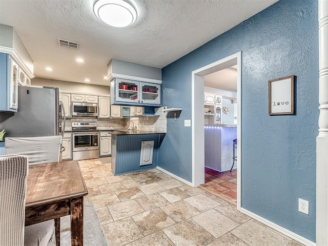 kitchen featuring white cabinetry, stainless steel appliances, a textured ceiling, decorative backsplash, and kitchen peninsula