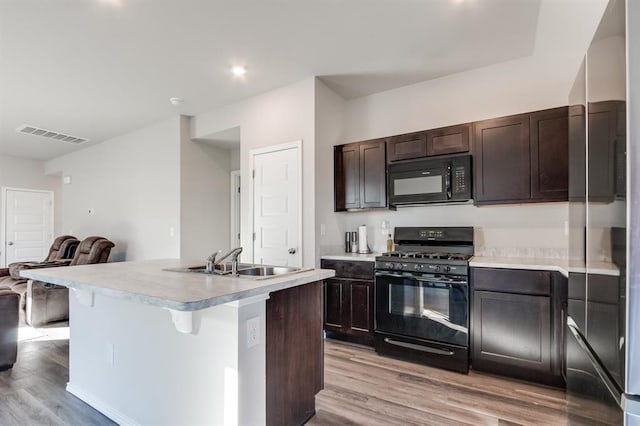 kitchen featuring sink, dark brown cabinetry, light hardwood / wood-style floors, black appliances, and an island with sink