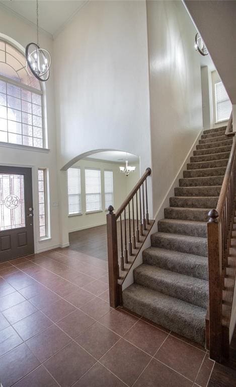 tiled foyer entrance with a towering ceiling, ornamental molding, and a notable chandelier